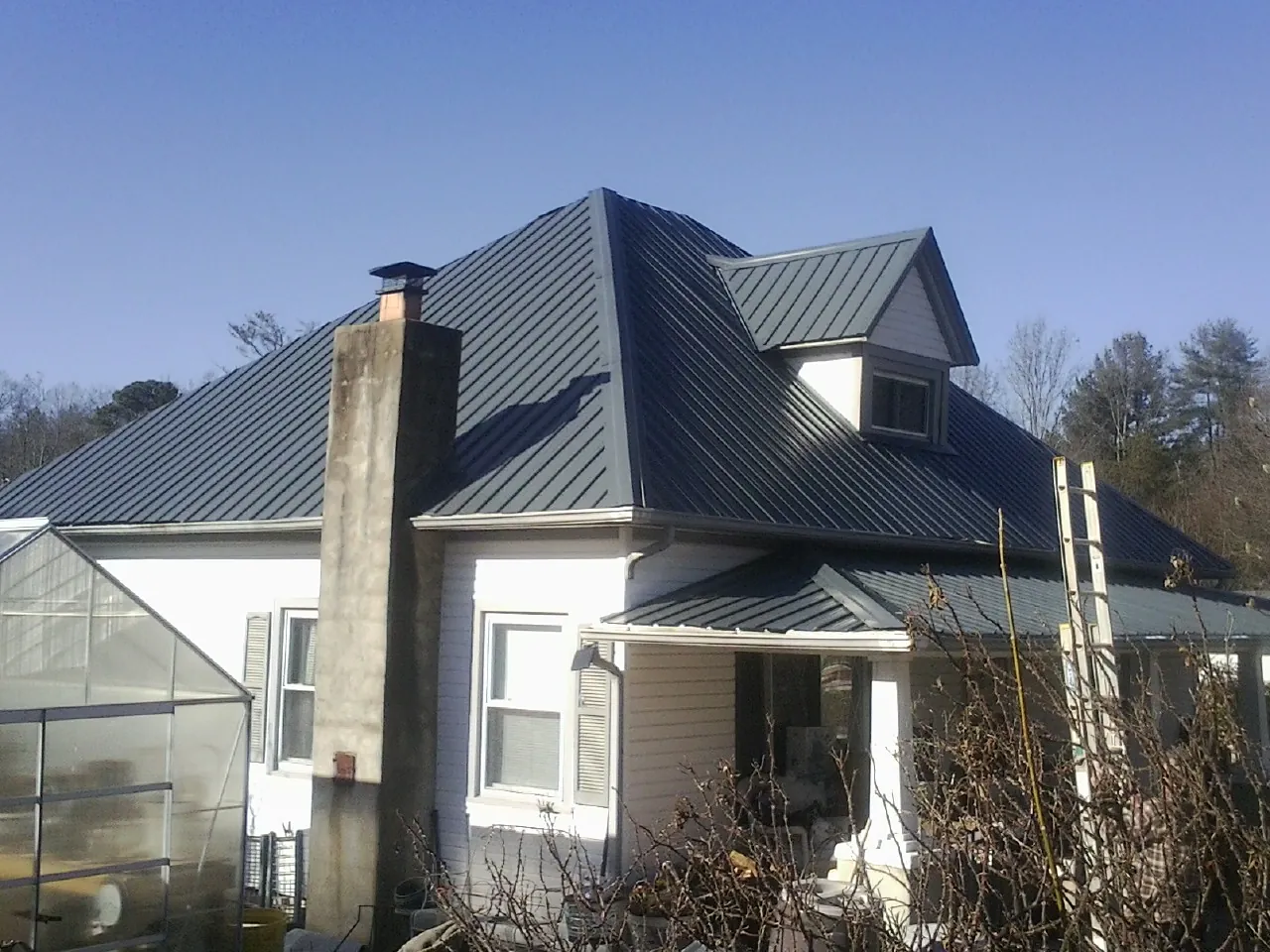 Dark blue standing seam metal roof on a white farmhouse with dormer — Slate & Tile Roof Repair by Roofing Brothers in Cherry Point