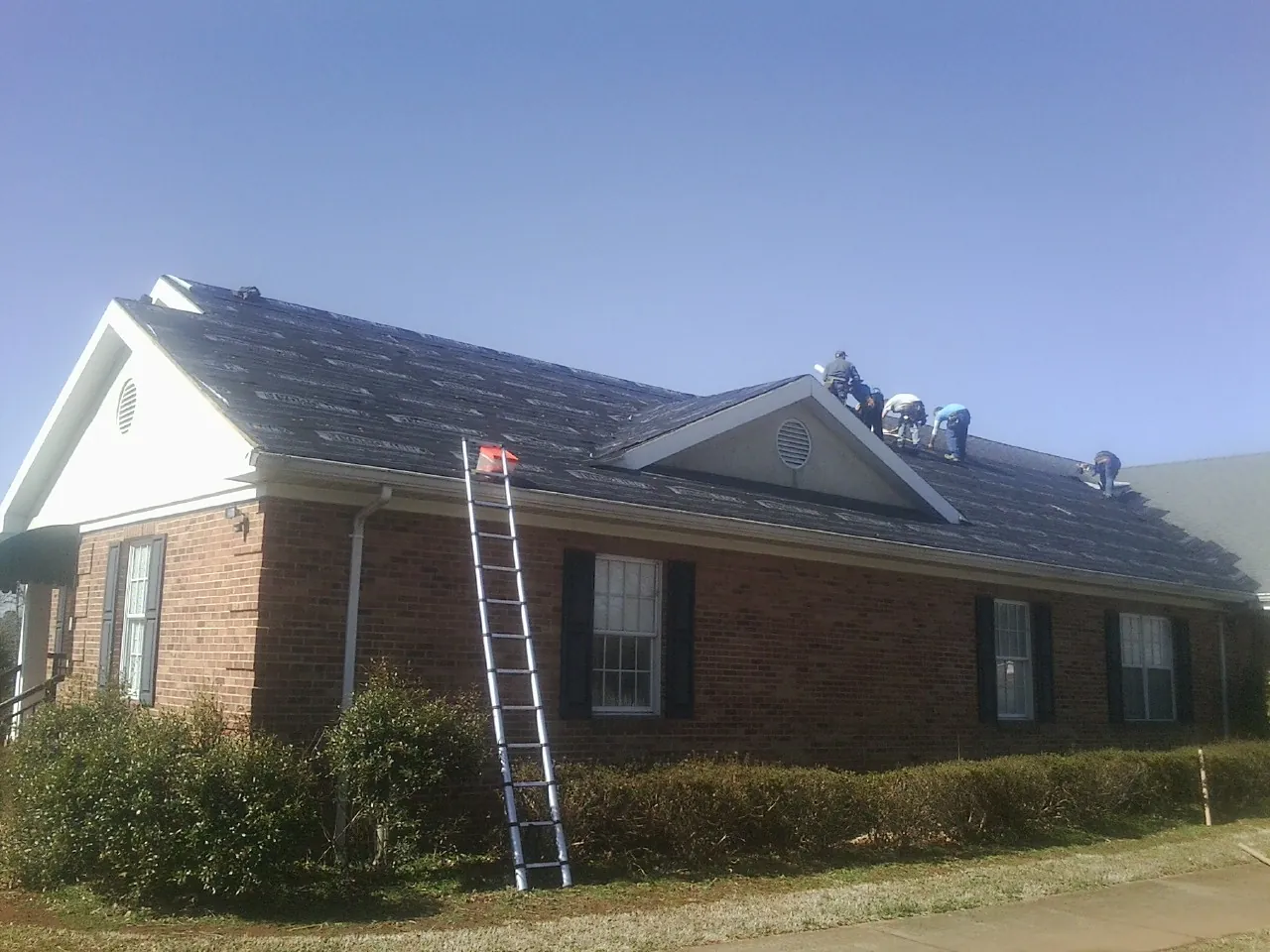 Crew tearing shingles off a brick ranch roof with a ladder set — Metal Roof Repair work by our crew in Cherry Point
