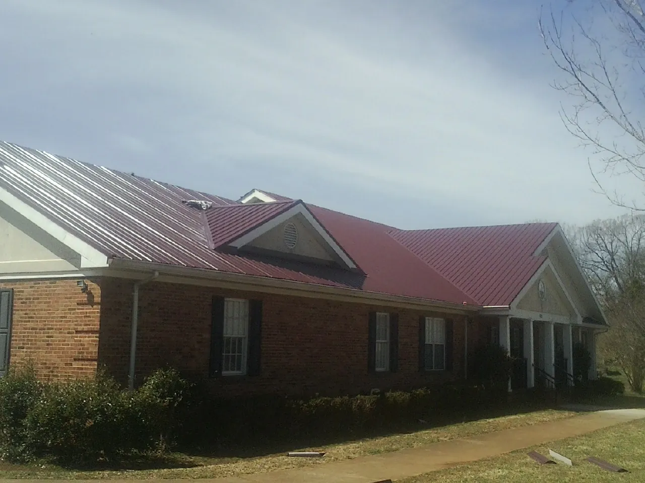 Red metal roof with gabled entries on a long brick building, from a Hail Damage Roof Repair job in Cherry Point