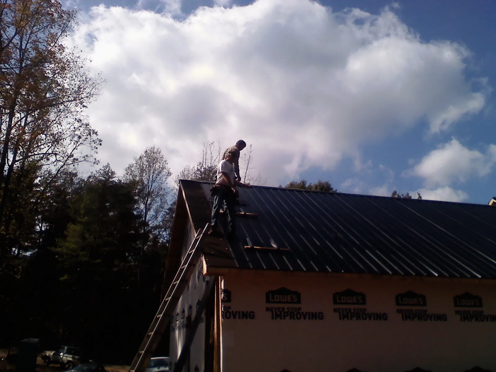 Roofer fastening dark metal panels high against a cloudy sky, from a Roof Inspection job in Cherry Point